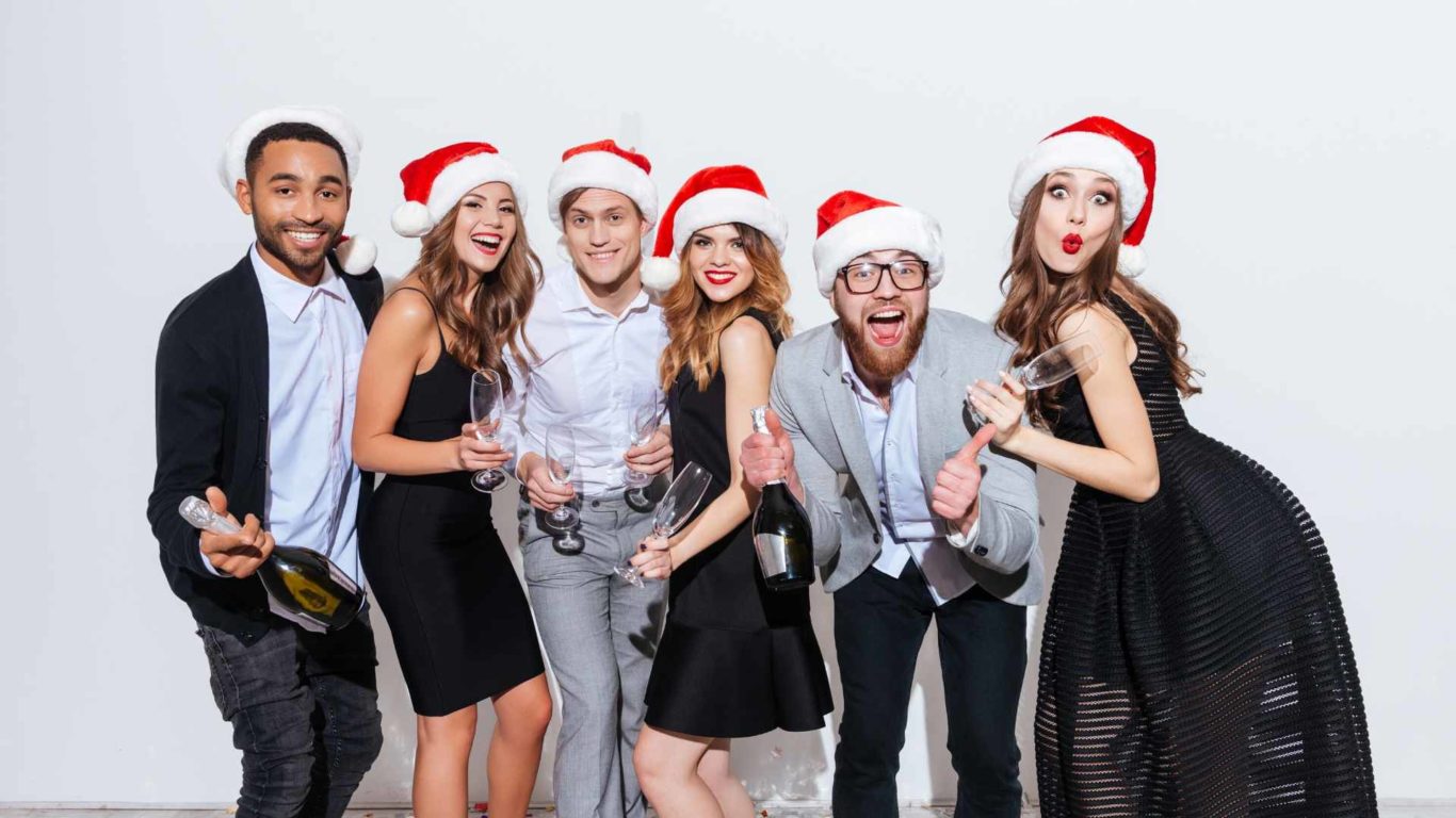 Image of 3 women and 3 men wearing Santa hats, holding champagne flutes and laughing