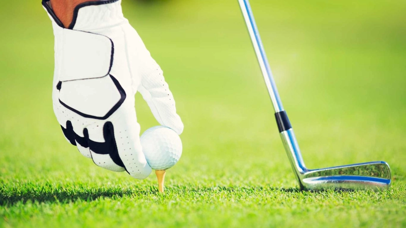 Close-up of man on a green golf course with golfing glove, placing golf ball on tee next to a golf club