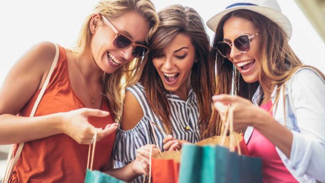 Three women with sunglasses looking excitedly at shopping bags